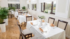 A dining area with multiple tables set for a meal, featuring white tablecloths, neatly arranged cutlery, and potted plants. - Arkadia (Warsaw)