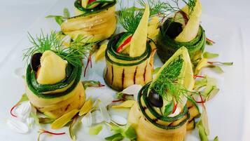 Un plato blanco con cinco porciones de comida, cada una con forma de torre, adornado con hojas verdes y detalles rojos.