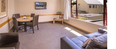 Habitación de hotel con comedor, sofá, televisión y ventana con vistas a edificios.