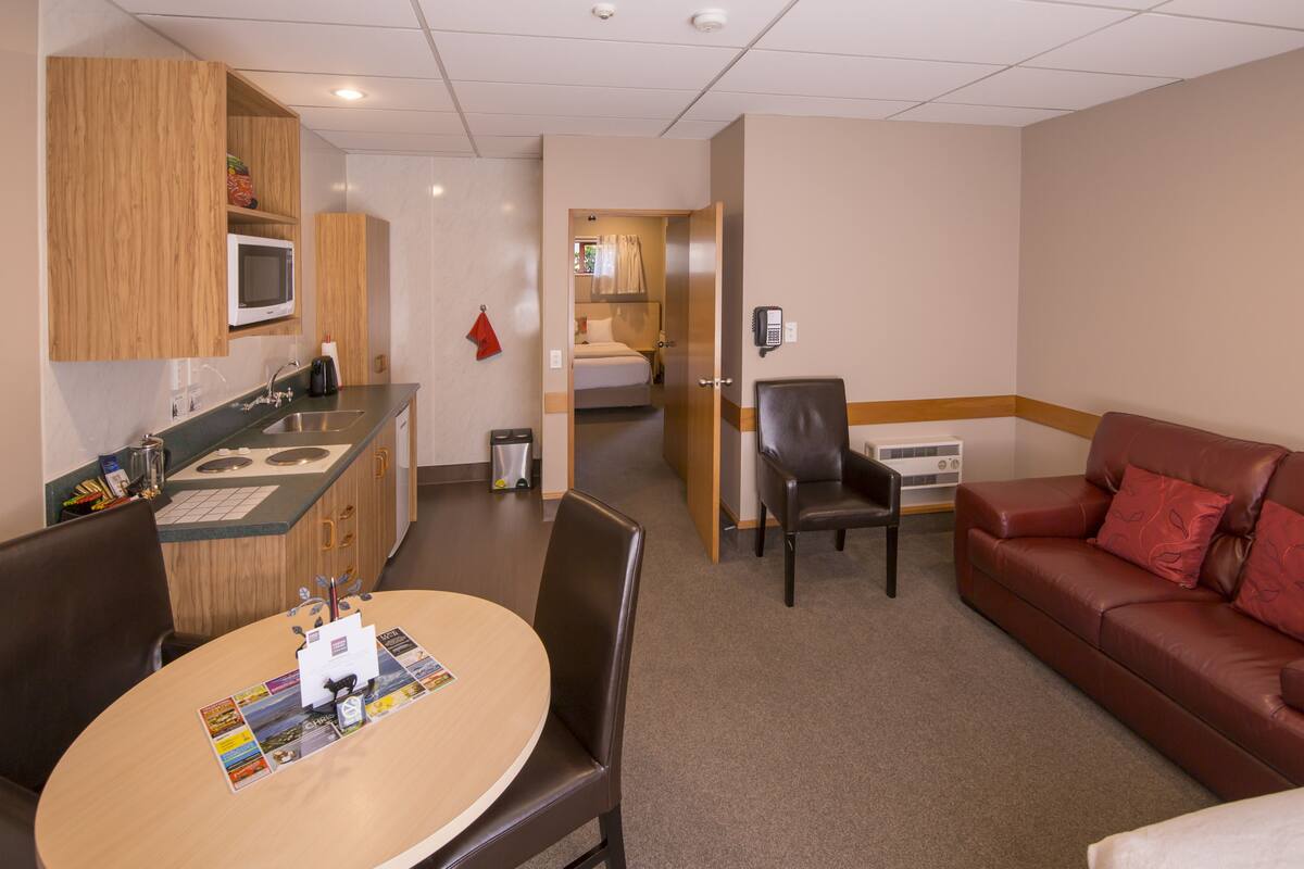 Habitación de hotel compacta con kitchenette, comedor, sofá y una cama individual.