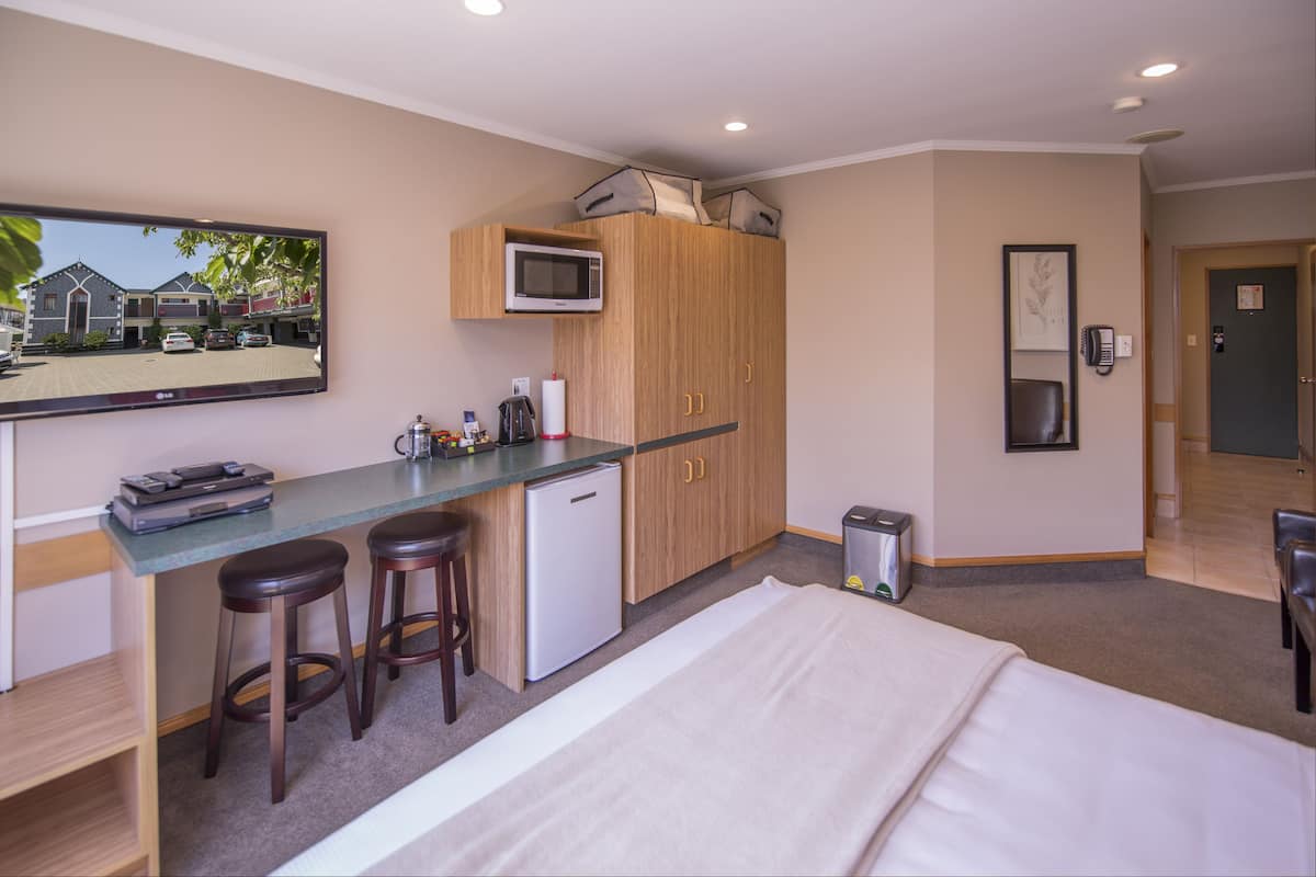 Habitación de hotel compacta con kitchenette, cama, un espejo grande y vista a la calle.