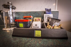 Una encimera de cocina con una cafetera, un molinillo de café y una cesta con productos para el desayuno y barras de chocolate.