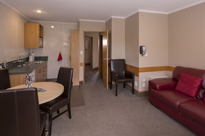 A compact living space with a kitchenette, a dining area, and a seating area with a red sofa. - Amross Court Motor Lodge (Christchurch)
