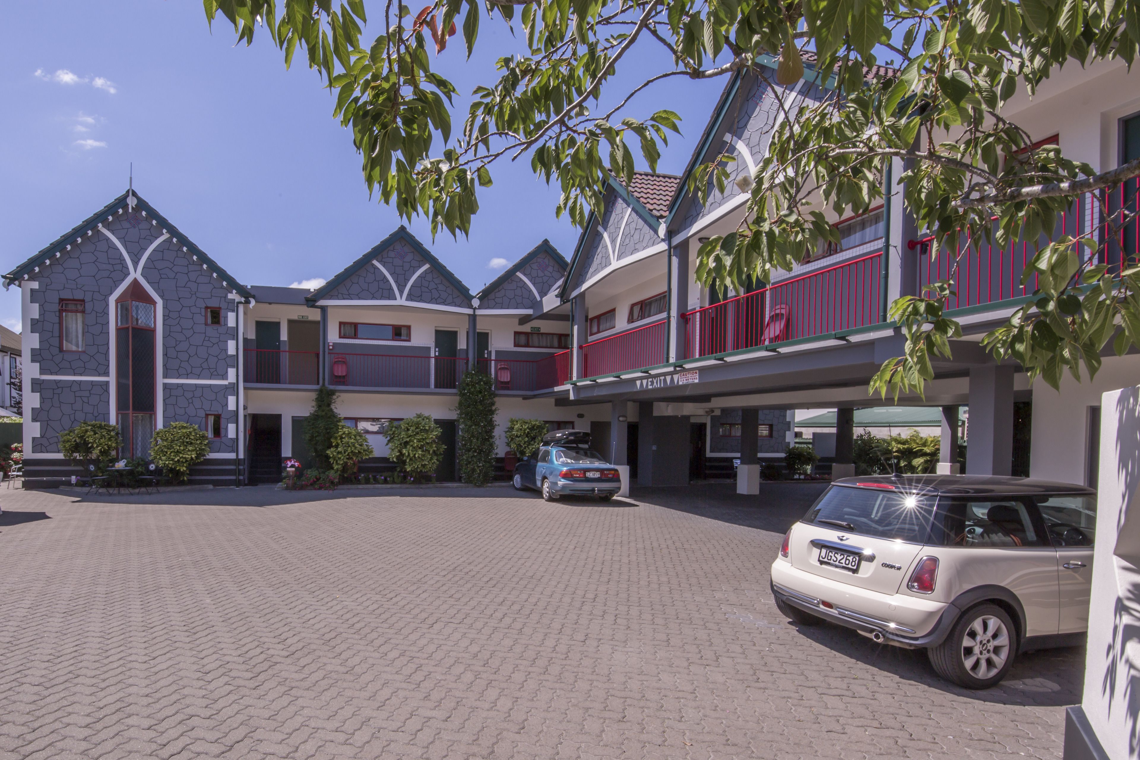 A hotel with a paved courtyard, multiple buildings with balconies, and a parked car.