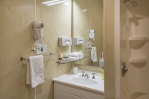 A modern bathroom with a large mirror, a sink, a towel rack, a hairdryer, and a glass shelf with toiletries.