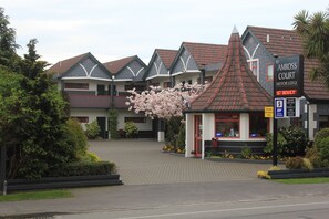 A building with a sign for Amross Court Motor Lodge, featuring a red roof, stone accents, and a small kiosk with a red door.