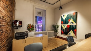 A conference room with a wooden table, a black office chair, a printer, and a television on a shelf.