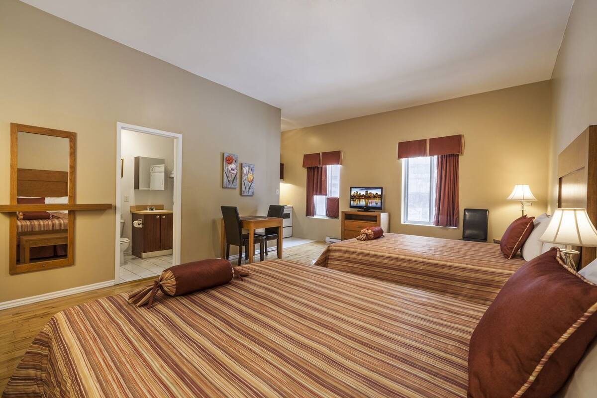 A hotel room with two beds, a desk, a television, and a bathroom.