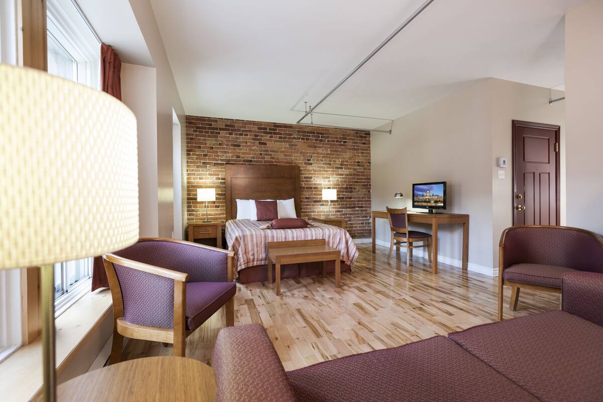A hotel room with a brick wall, a bed, a desk, and two chairs.