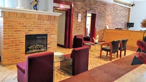 A spacious lobby with a brick fireplace, red upholstered chairs, and a wooden reception desk.