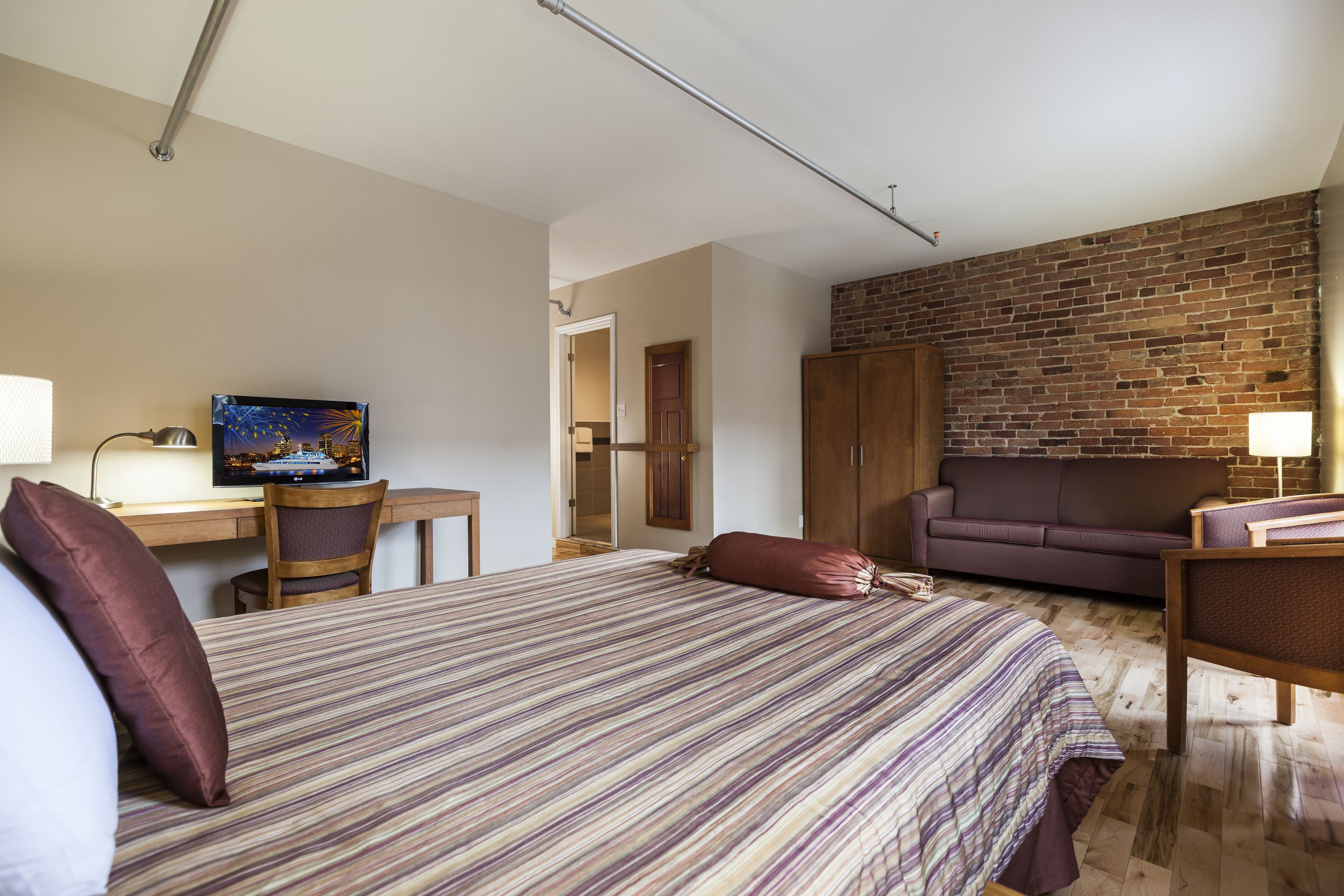 A hotel room with a bed, a desk, a television, a couch, and a brick wall.