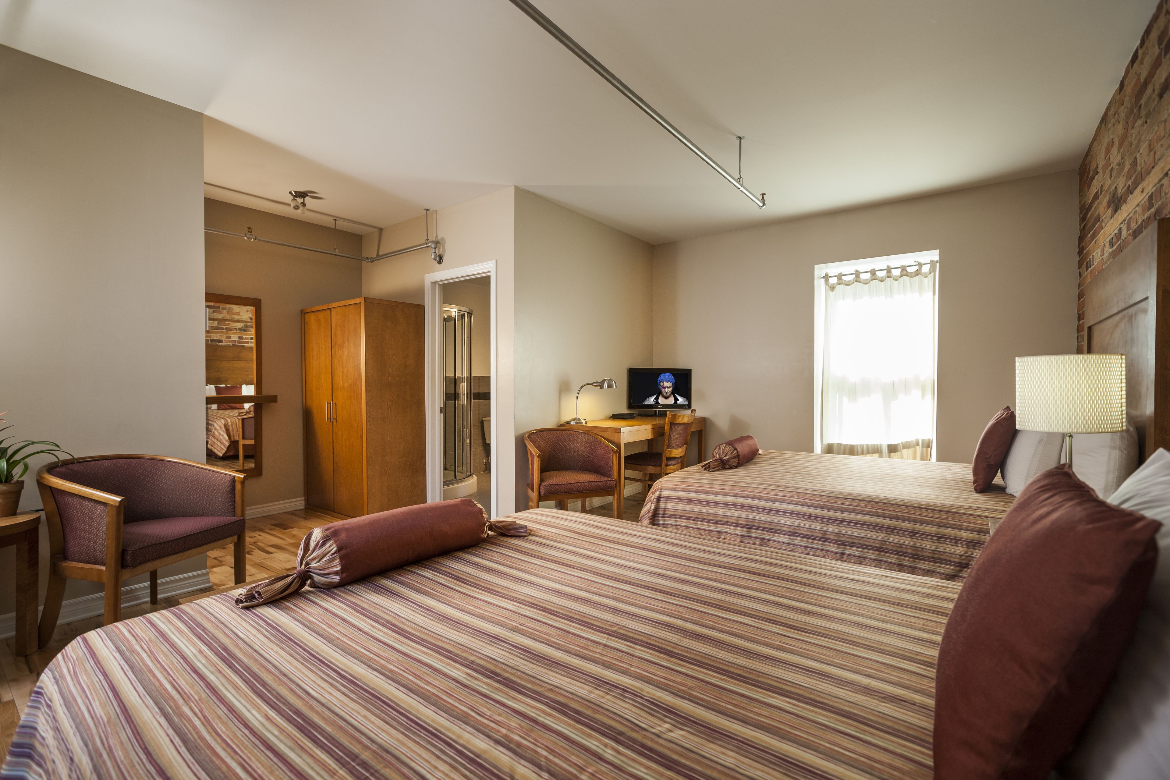 Habitación de hotel con dos camas, un escritorio con silla, televisión y ventana con cortinas.