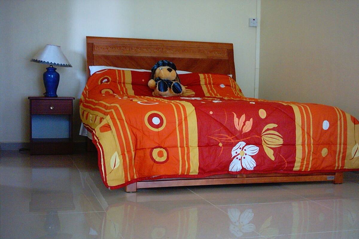 Ein Bett mit floralem Überwurf, ein Nachttisch mit Lampe und eine kleine Schublade.