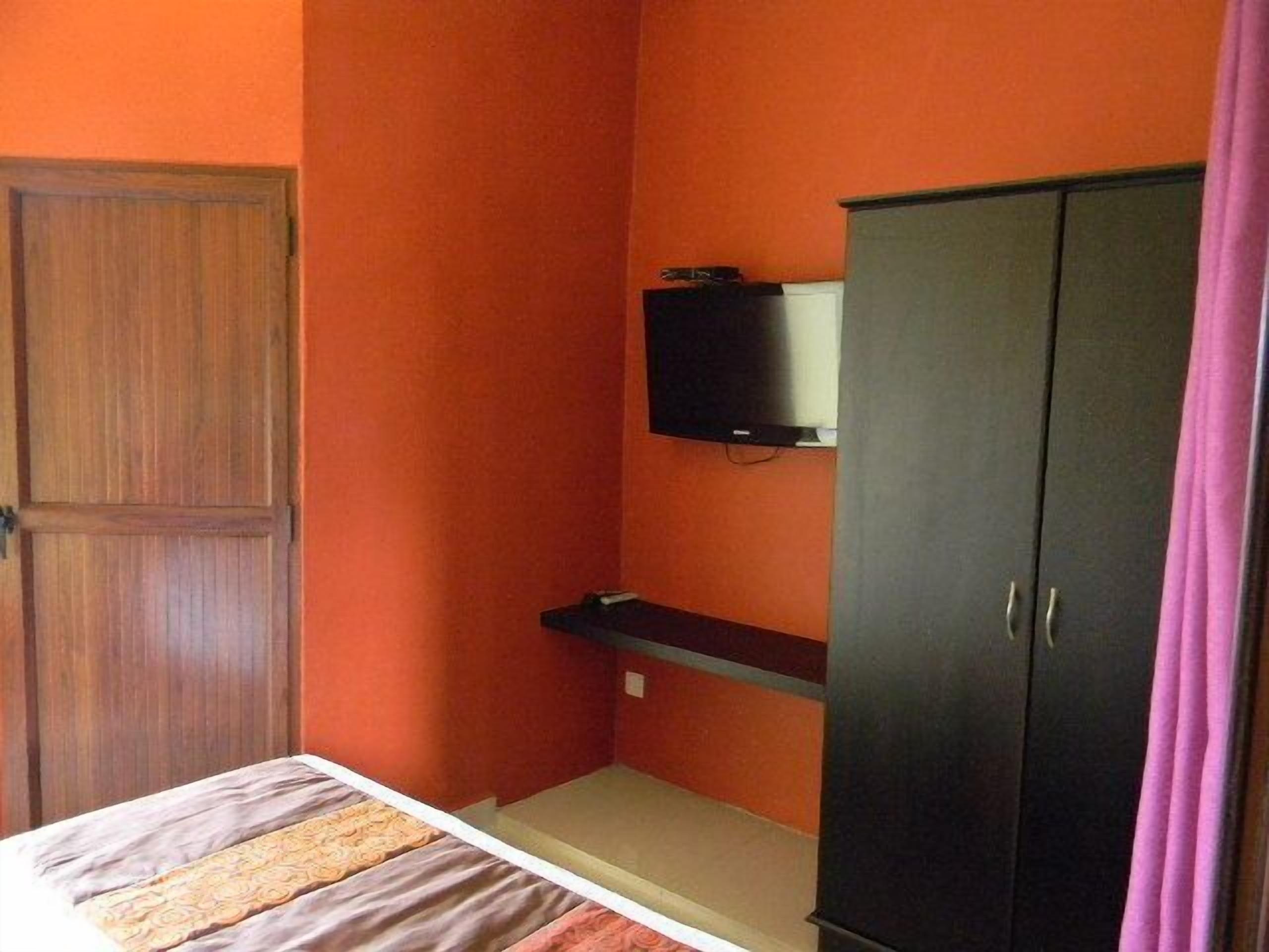 Een kamer met een bed, een kledingkast, een aan de muur bevestigde televisie en een roze gordijn.