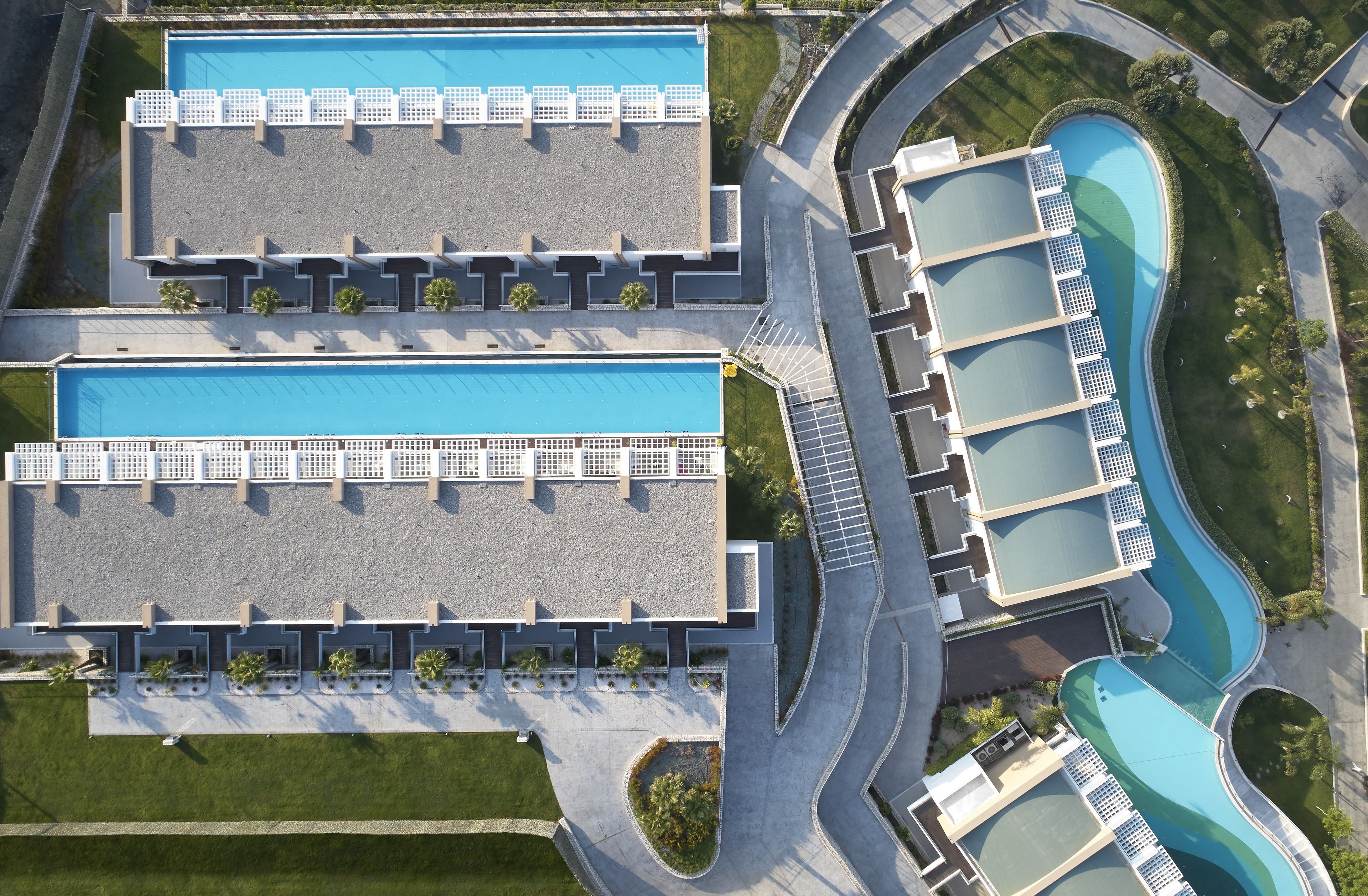 Vue aérienne d’un hôtel doté de deux grandes piscines, d’un jardin aménagé et d’un parking.