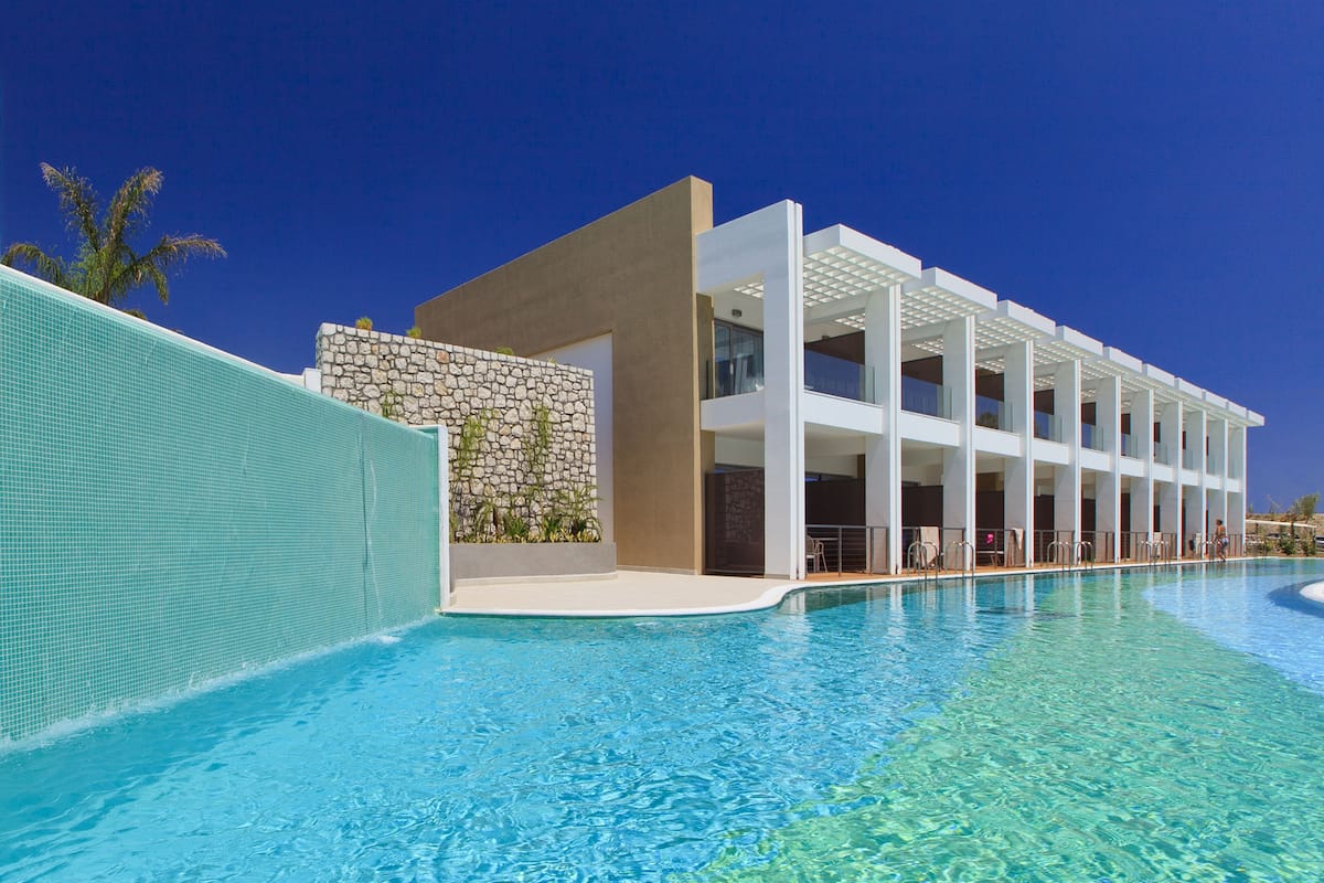 Hotel moderno com piscina, fachada de pedra e várias varandas.