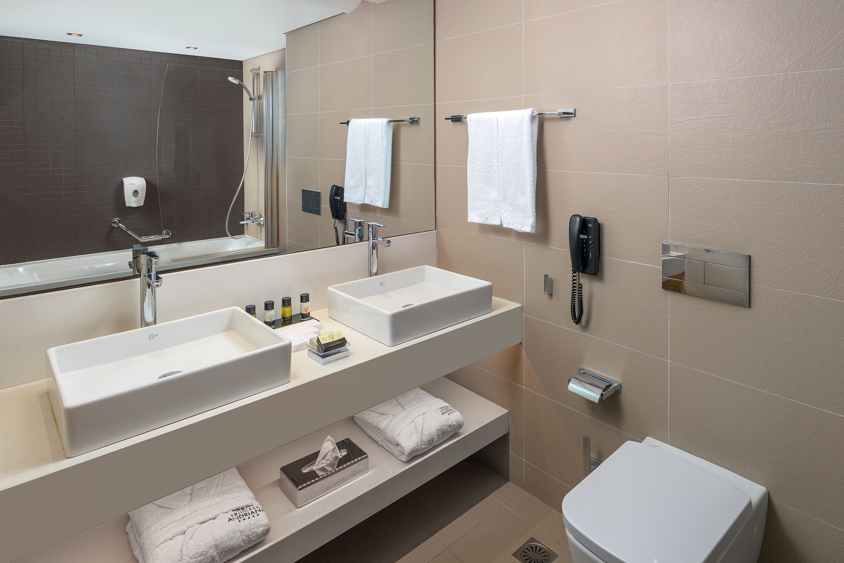 A modern bathroom with two sinks, a large mirror, a shower, and a toilet.