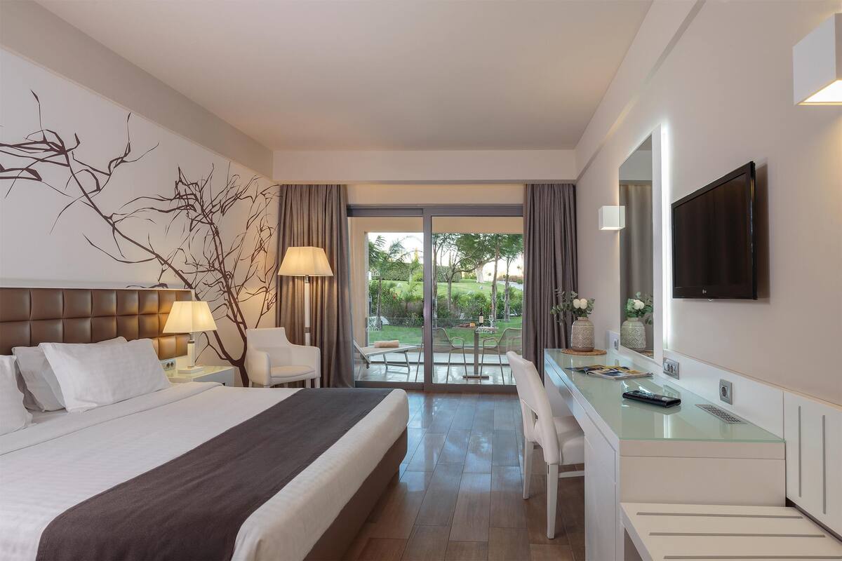 Quarto de hotel com cama, escrivaninha e vista para a área externa.