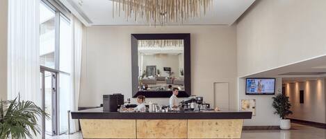 A modern hotel lobby with a reception desk, large mirror, and a television screen.