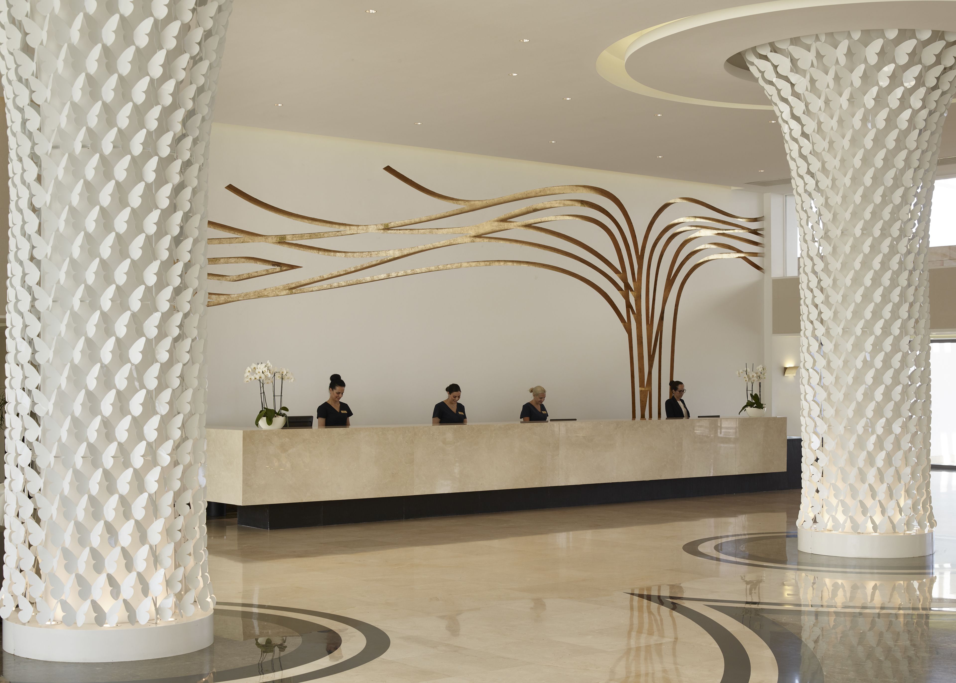 A modern reception area with a marble counter, three receptionists, decorative wall art, and large columns.