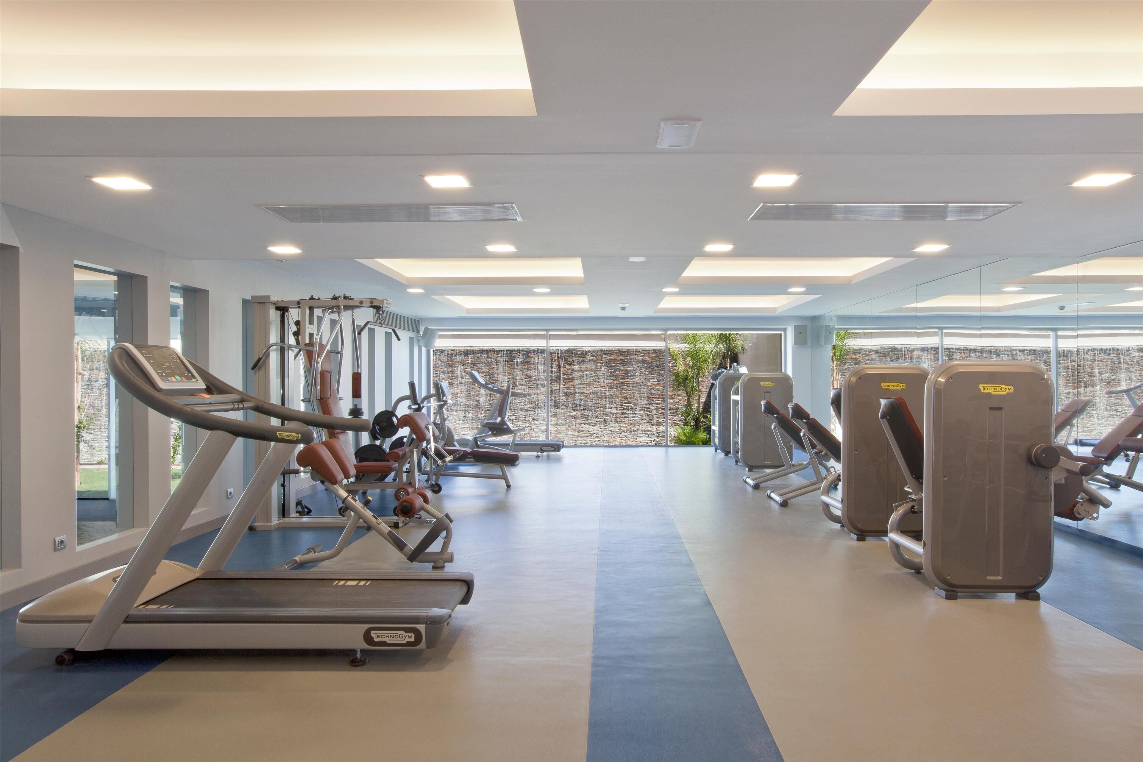 Ein modernes Fitnessstudio mit Laufbändern, Kraftgeräten und einem großen Fenster mit Blick auf die Stadt.