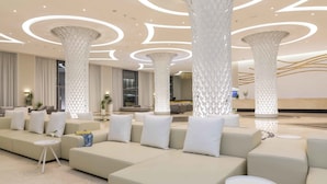 A modern lobby with a central seating area, large decorative columns, and a reception desk. - Princess Andriana Resort & Spa – Ultra All Inclusive (Rhodes)