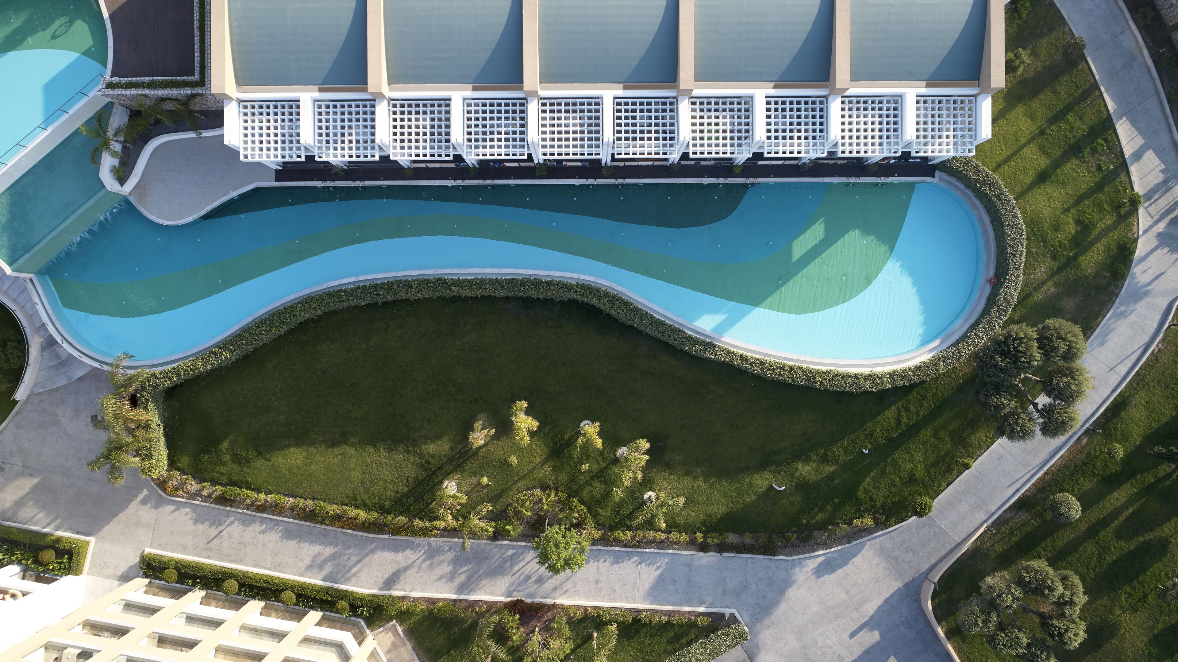 Ovenfra set et moderne hotel med en stor swimmingpool, anlagte haver og en mangeetagers bygning med et unikt arkitektonisk design.