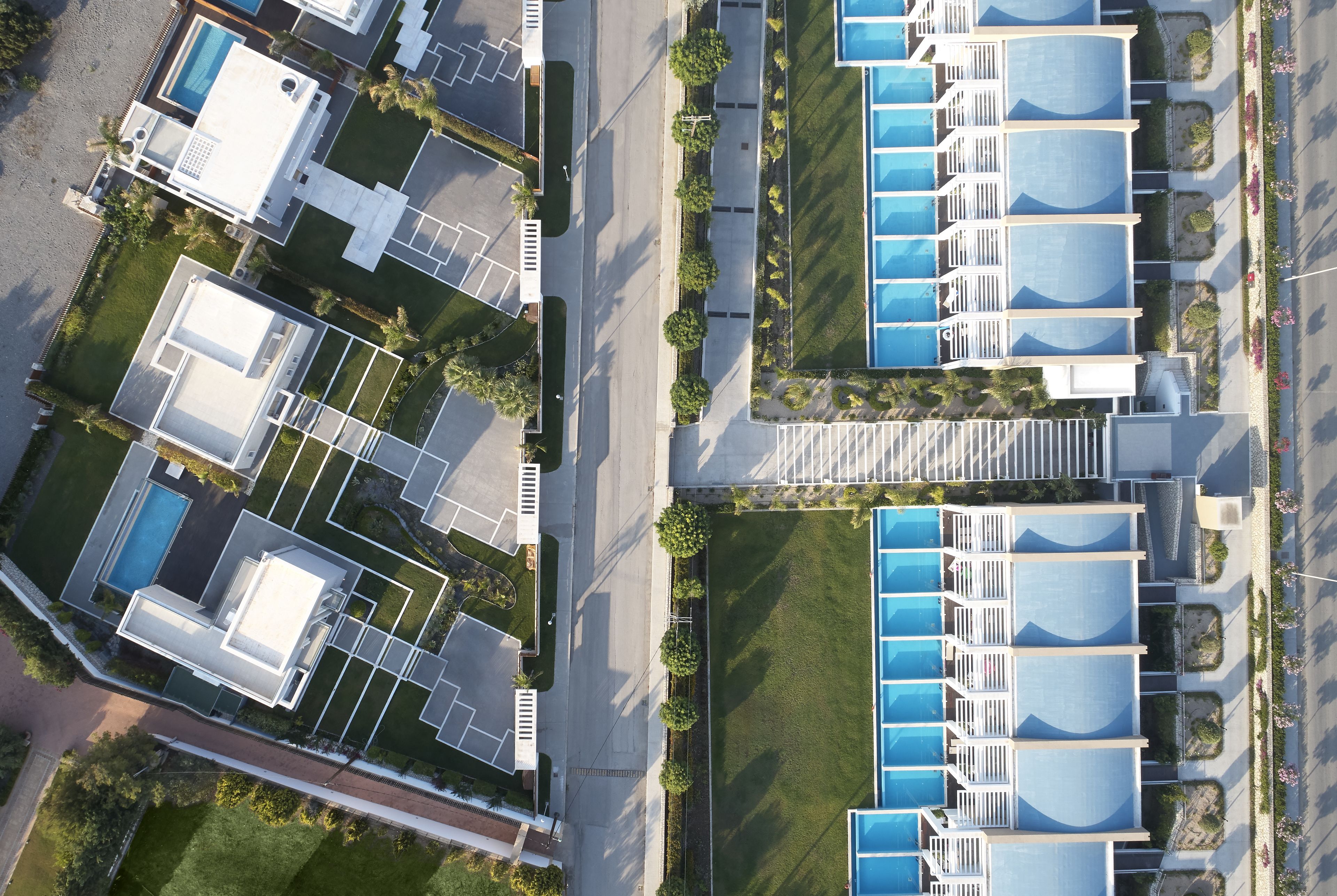 An aerial view of a modern hotel with multiple swimming pools, arranged in rows, and surrounded by well-maintained lawns and pathways.