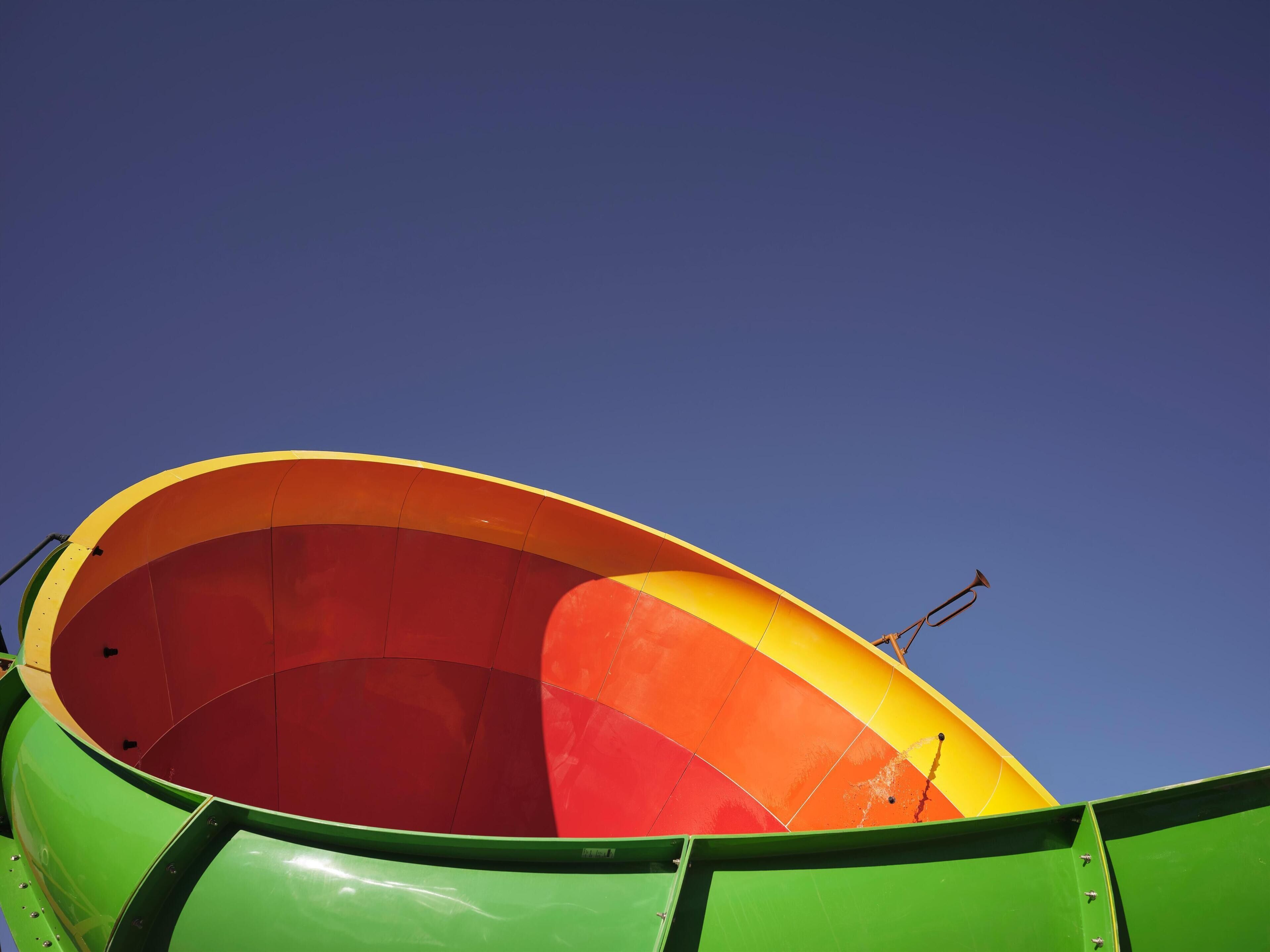 Una estructura grande, colorida y semicircular con fachada verde y interior amarillo y rojo, probablemente parte de un paseo de atracciones.