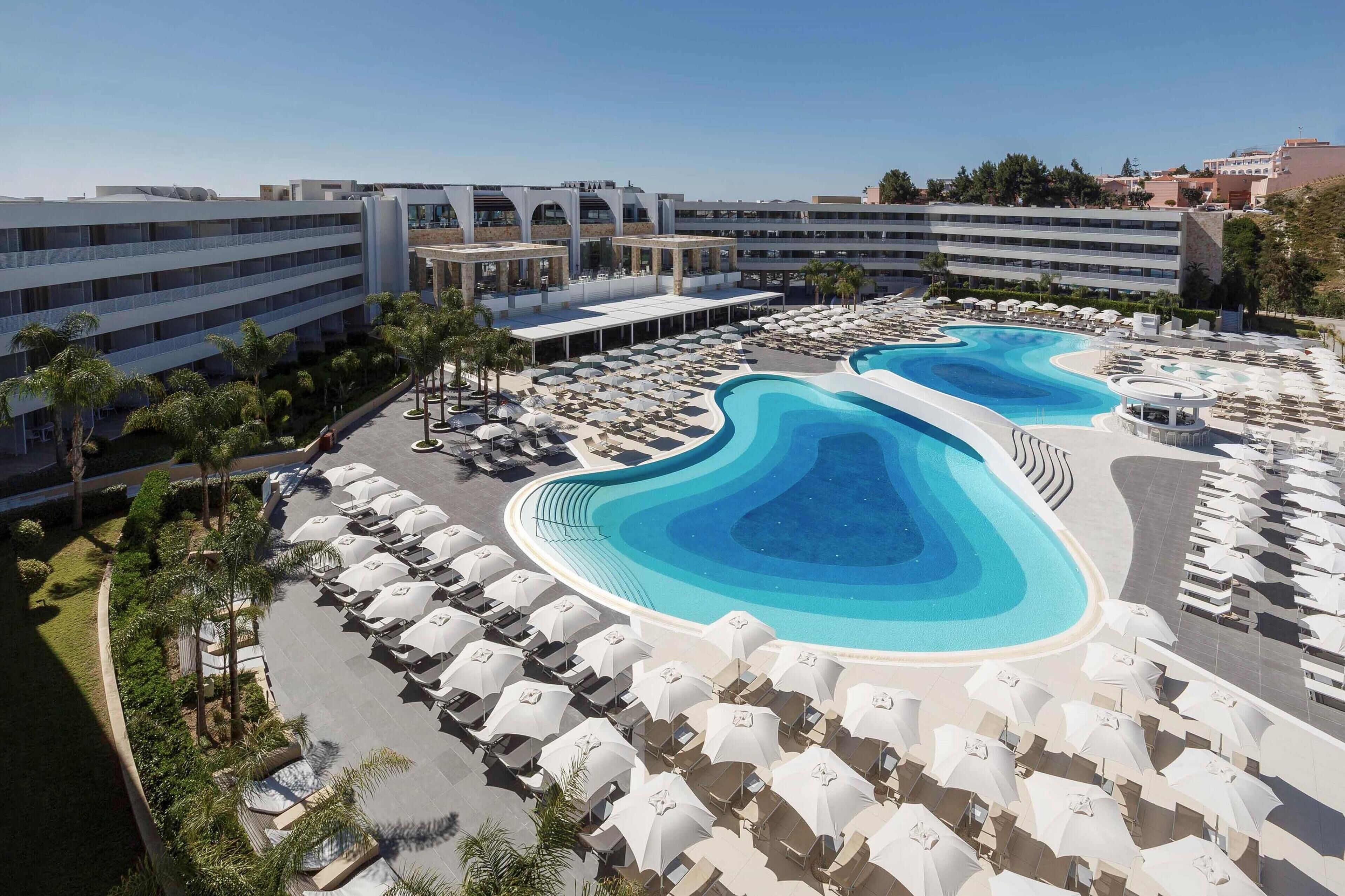 Un resort con un amplio espacio de piscina, numerosas tumbonas y una estructura de edificio moderna.