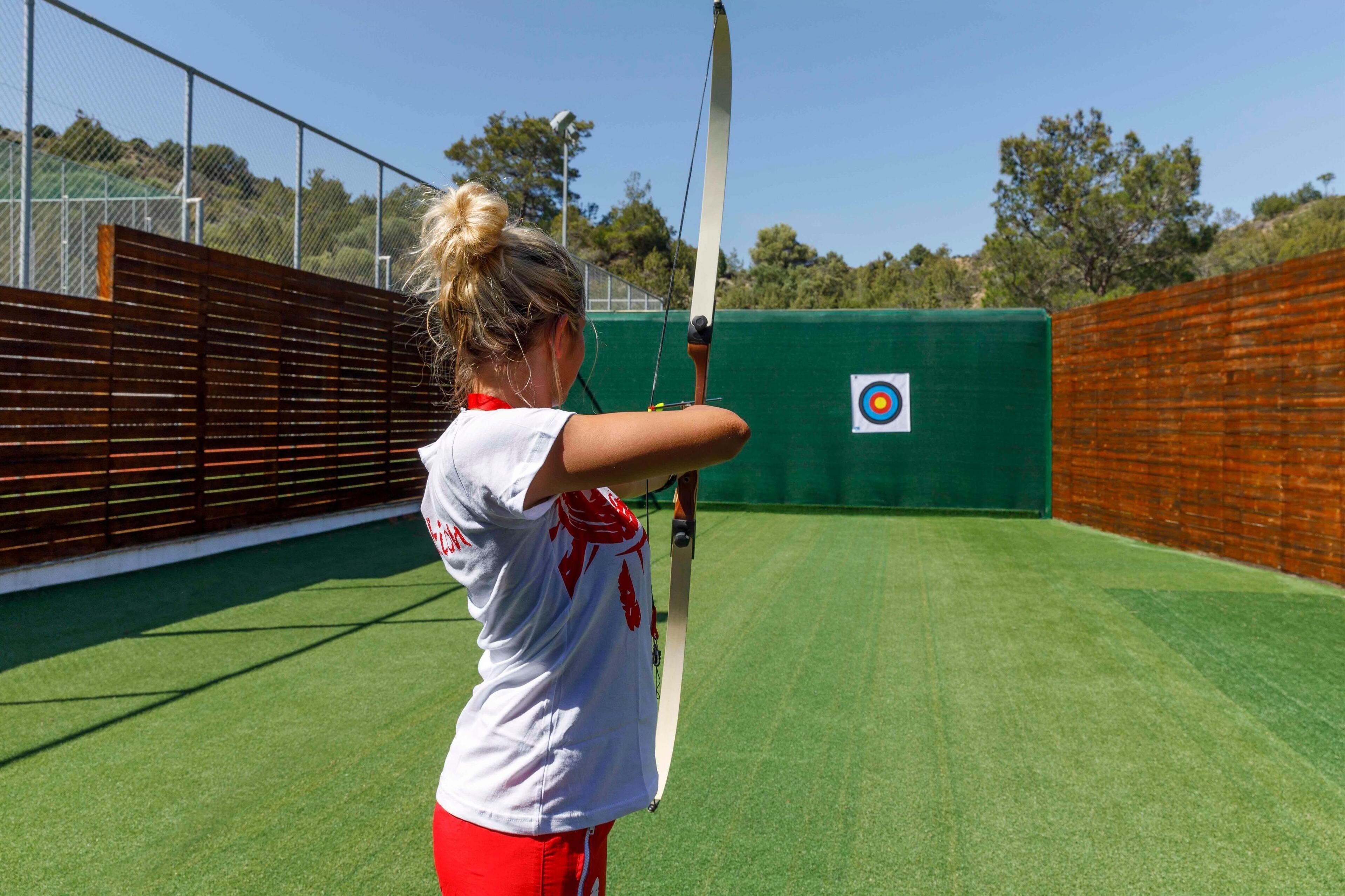 A person aiming a bow at a target in an outdoor archery range.