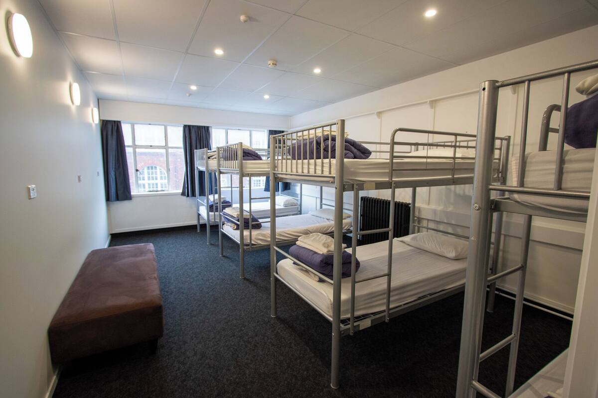 Un dormitorio con literas, un banco y una ventana con cortinas.