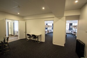 A spacious room with a carpeted floor, a white table with chairs, and a radiator. There are doors leading to other rooms.