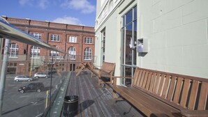 Un balcon avec des balustrades en bois, un bâtiment en briques en arrière-plan et un ciel bleu dégagé.