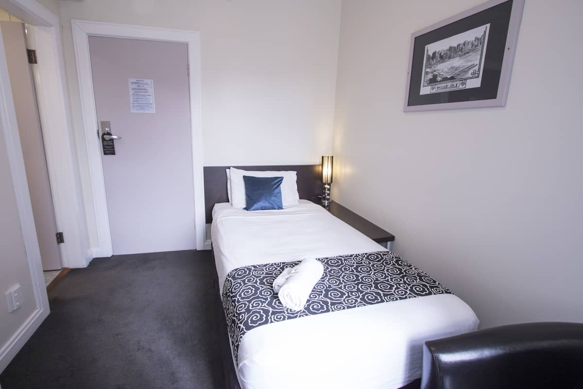 Habitación de hotel con cama, mesita de noche, lámpara, un cuadro en la pared y una puerta.