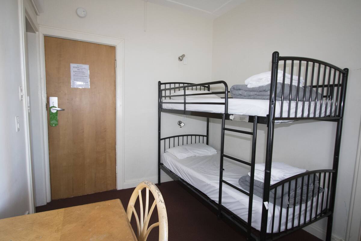 Habitación con literas, una puerta de madera, una mesita y una silla.