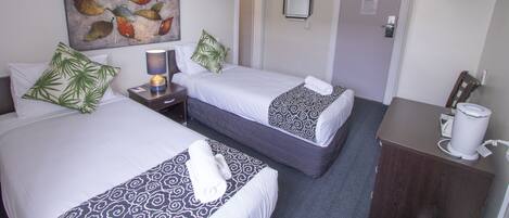 A hotel room with two beds, a TV, a coffee machine, and a painting on the wall.