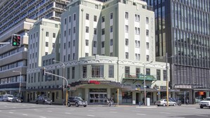Un hôtel au style architectural classique, reconnaissable à son enseigne « Hôtel Waterlo », à ses nombreux étages et à son emplacement d’angle donnant sur la rue.