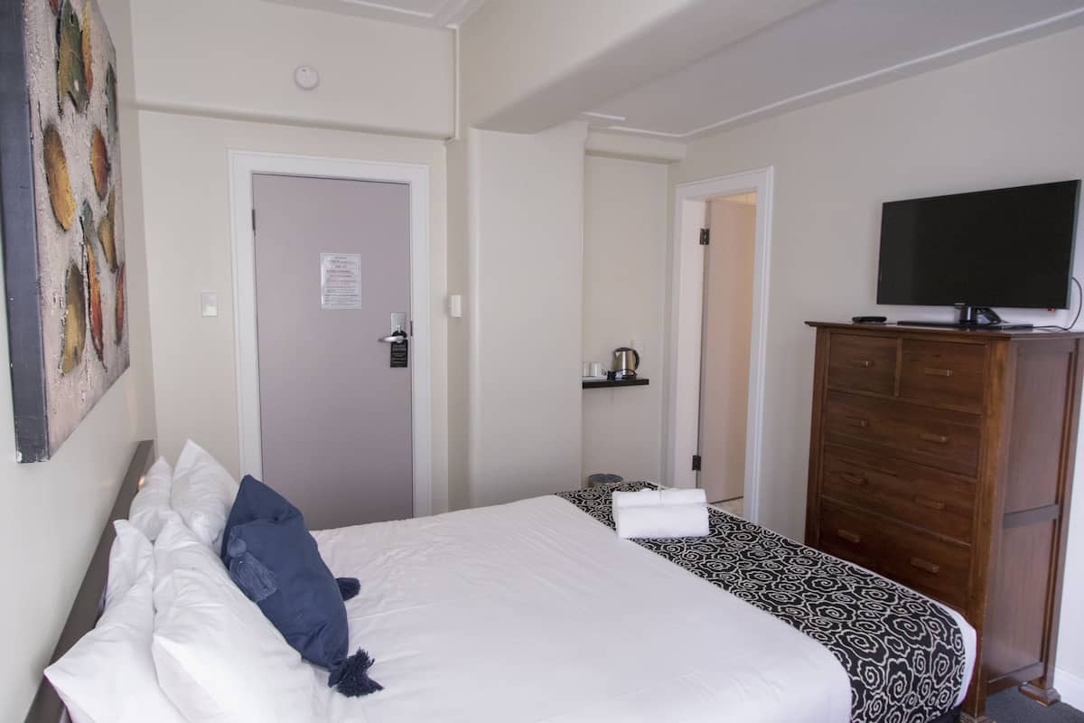 Una habitación de hotel con dos camas, televisión, cómoda de madera y un cuadro en la pared.