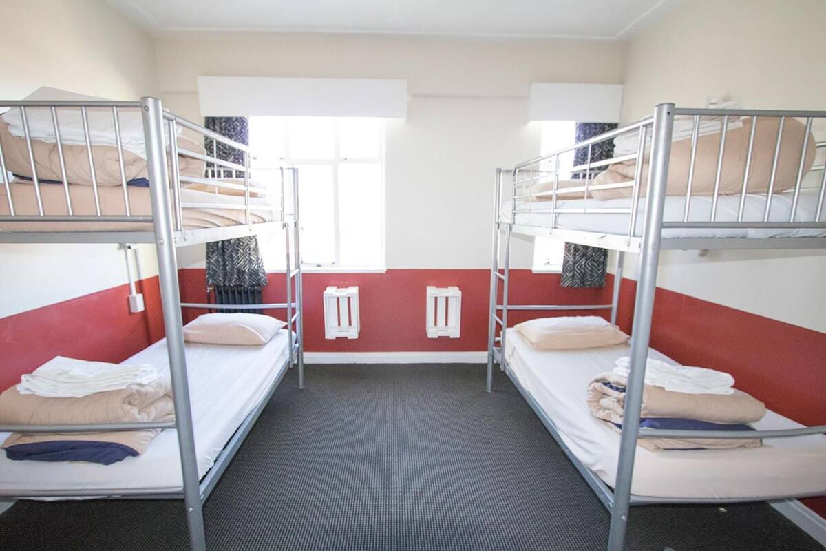 Un dormitorio con dos literas, una ventana con cortinas y un radiador.