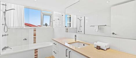 Un baño moderno con bañera, lavamanos y un espejo grande.