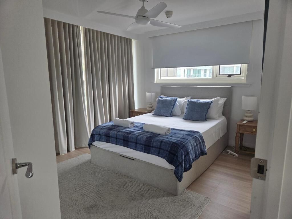 Et soveværelse med seng, ventilator, vindue og et natbord.