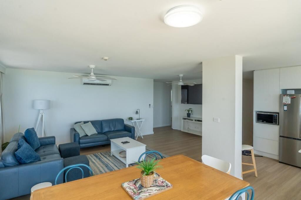 A modern living room with a sofa, a dining table with chairs, a small white table, and a ceiling fan.