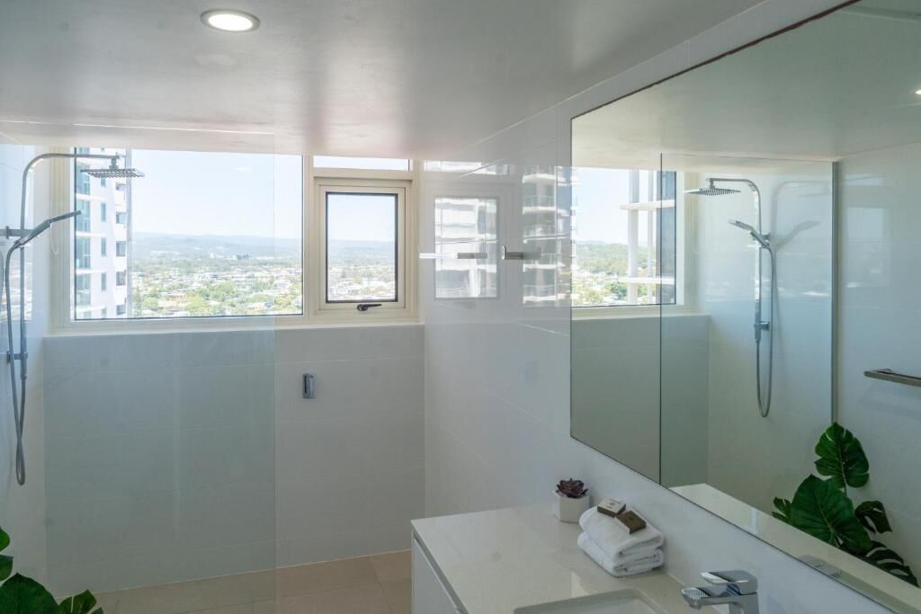 A modern bathroom with a large mirror, a shower, and a sink.