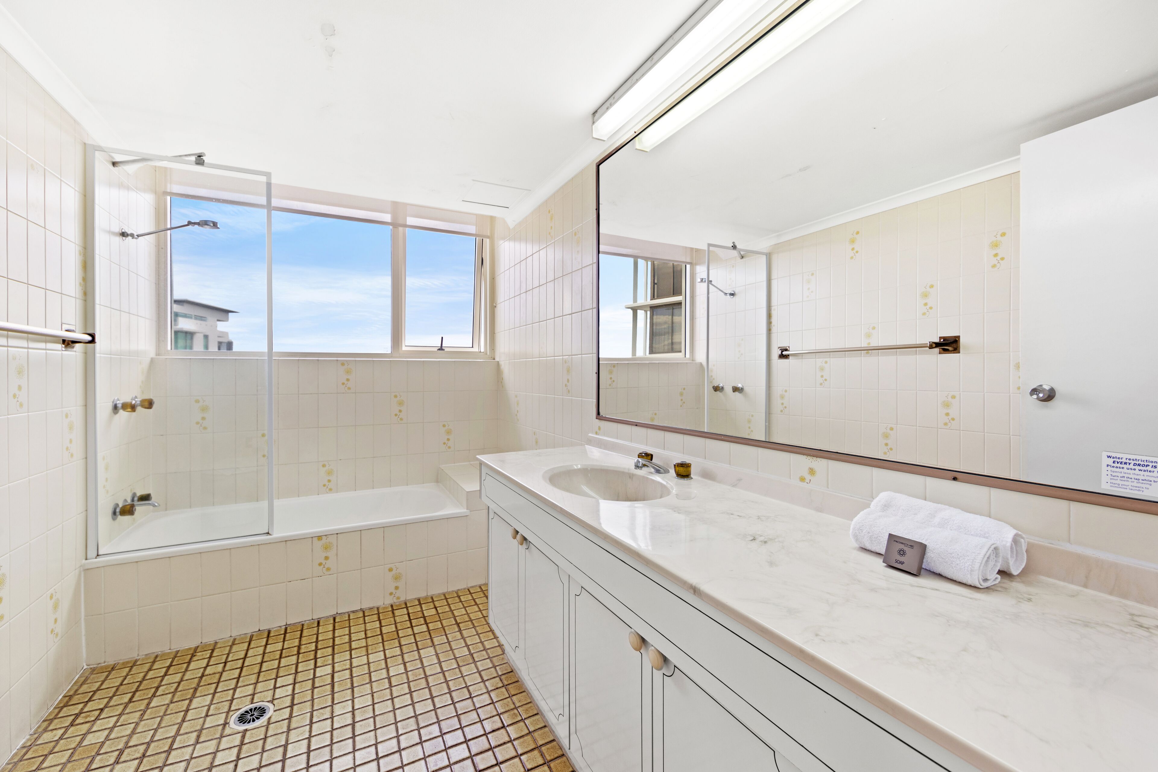 A modern bathroom with a large mirror, a bathtub, a shower, and a sink.