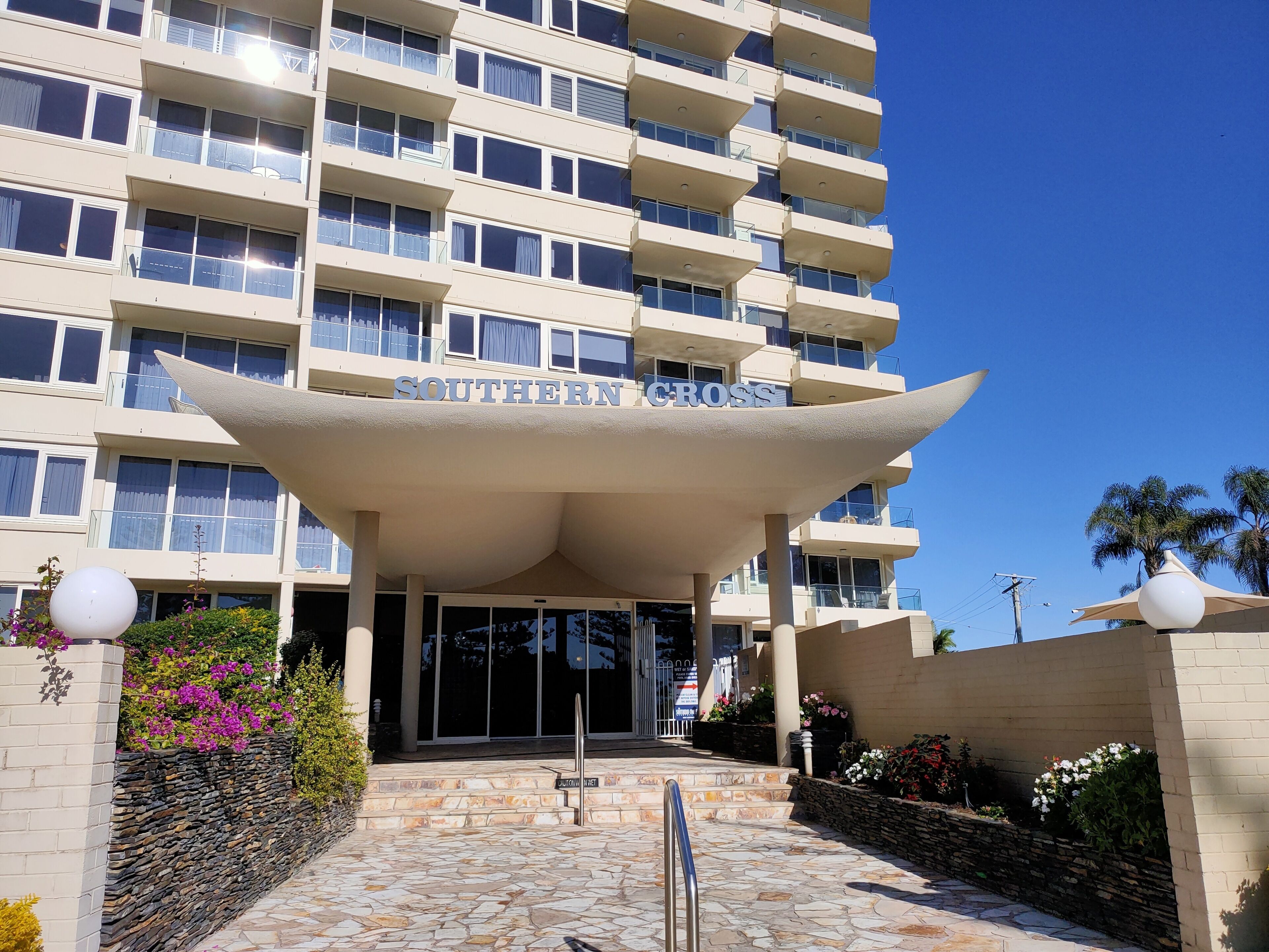 A multi-story hotel with a prominent entrance, a sign reading "SOUTHERN CROSS," and a stone-paved entrance area with steps.
