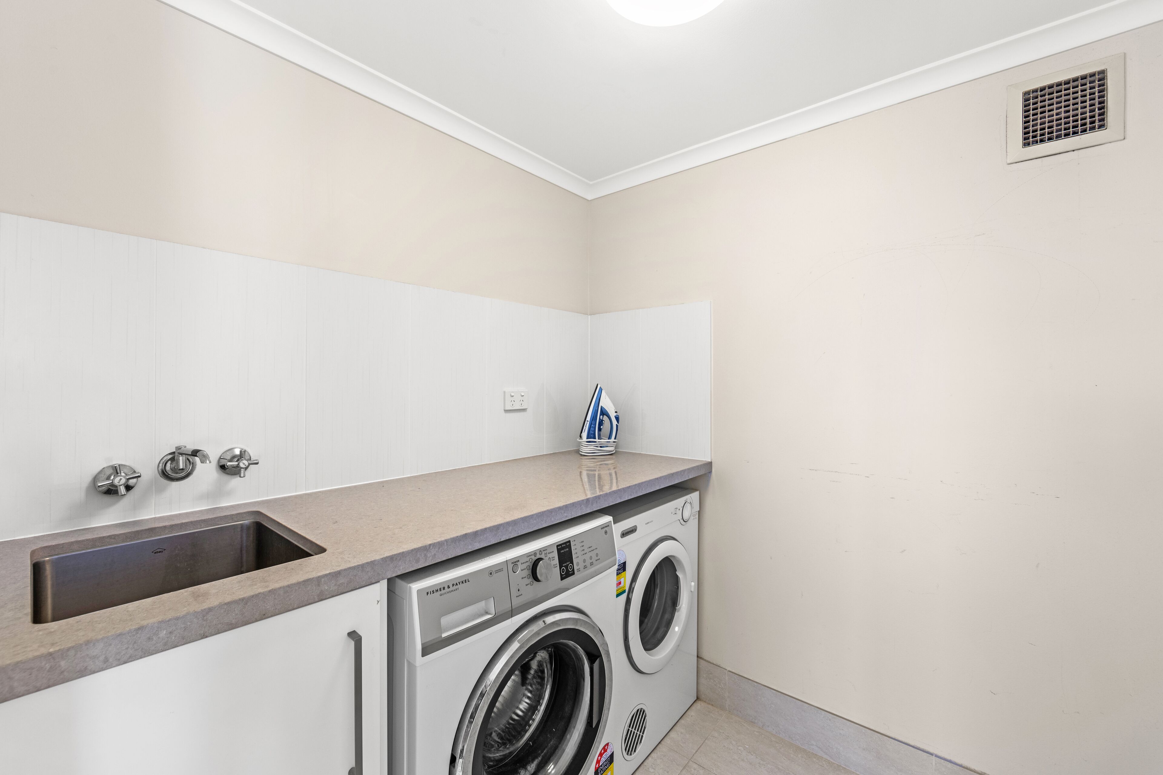 A laundry room with a built-in washer and dryer, a sink, and a countertop.