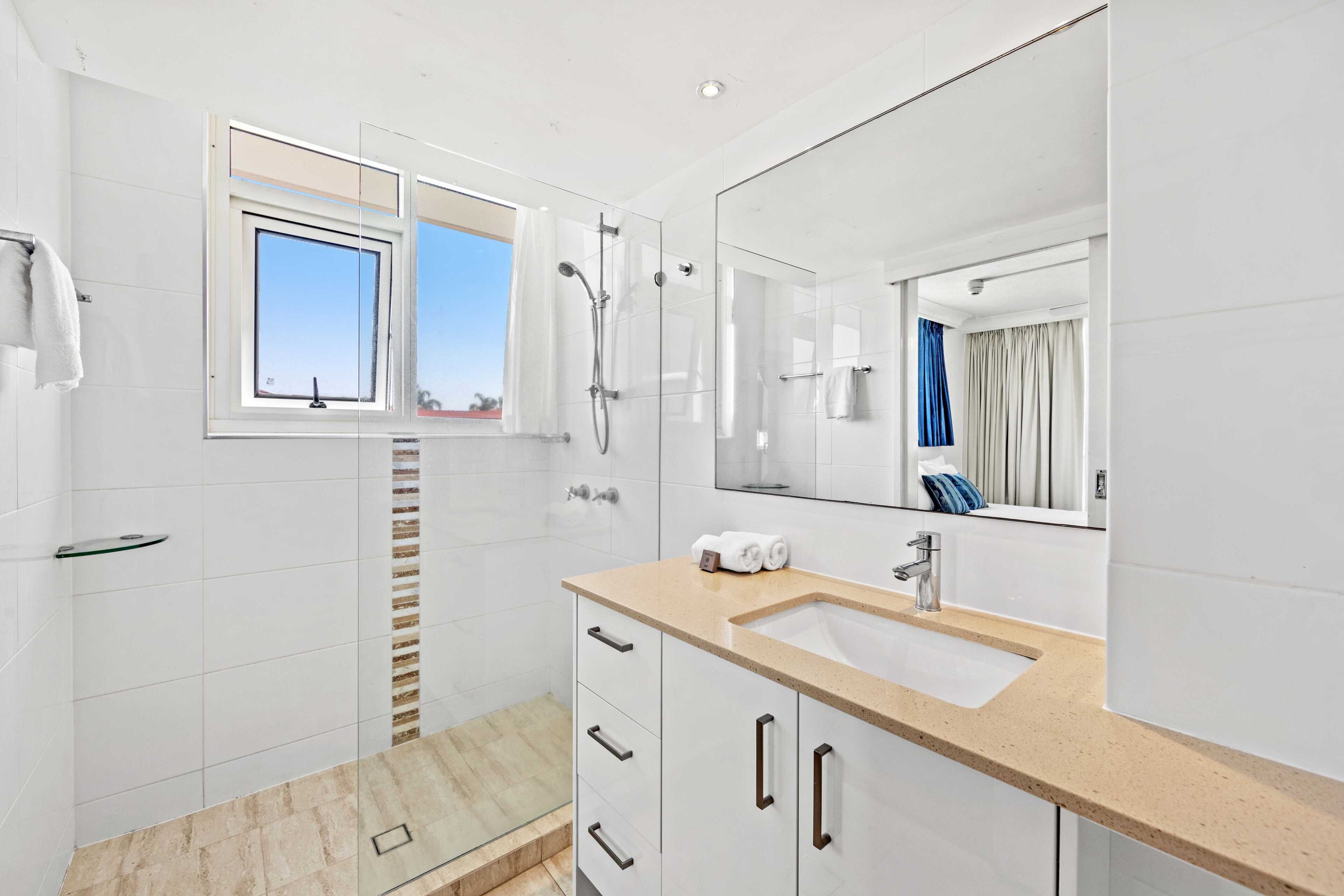Un baño moderno con un espejo grande, un lavamanos y una zona de ducha.