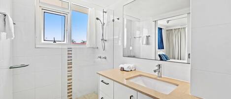 Un baño moderno con un espejo grande, un lavamanos y una zona de ducha.