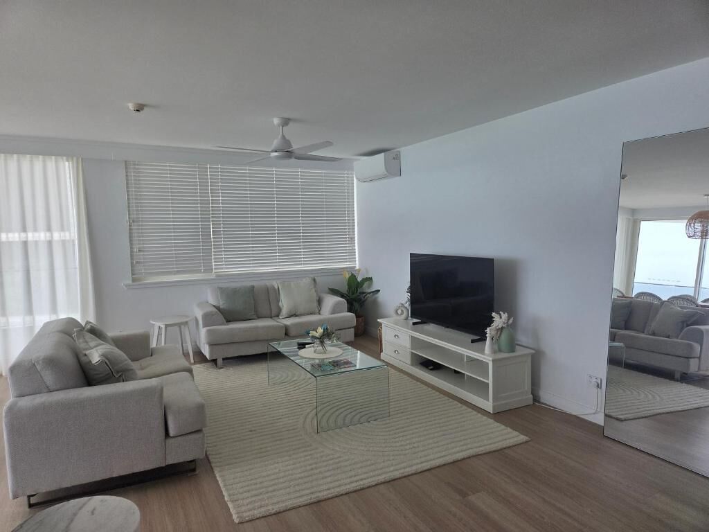 A modern living room with a sofa, coffee table, TV, and a large window with blinds.